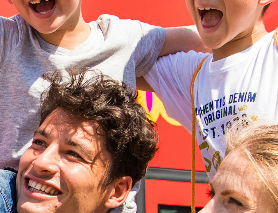 A cheerful family of four takes a selfie in front of a red double-decker tour bus.