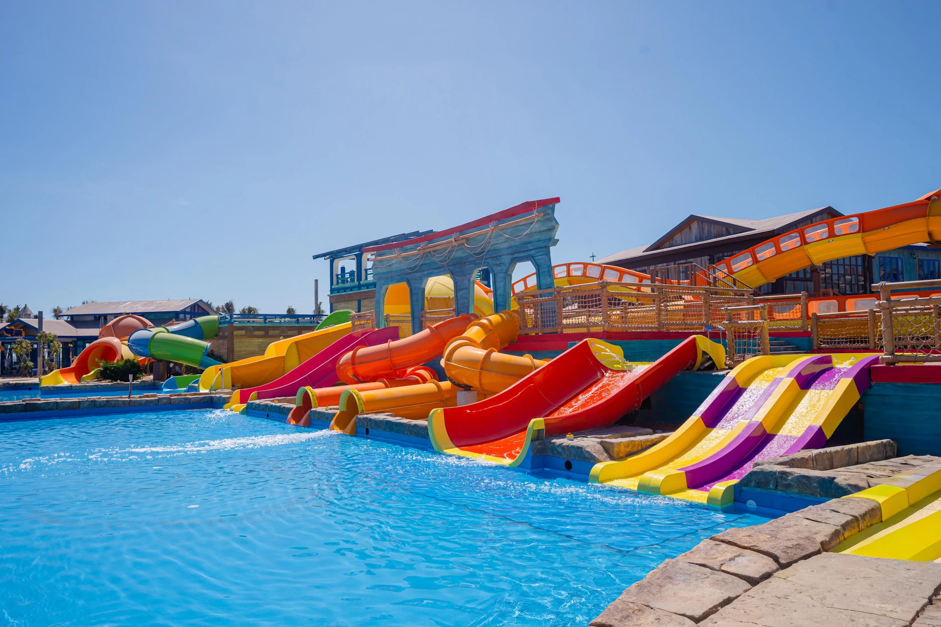 A water park with colorful slides leading into a blue pool under a clear sky.