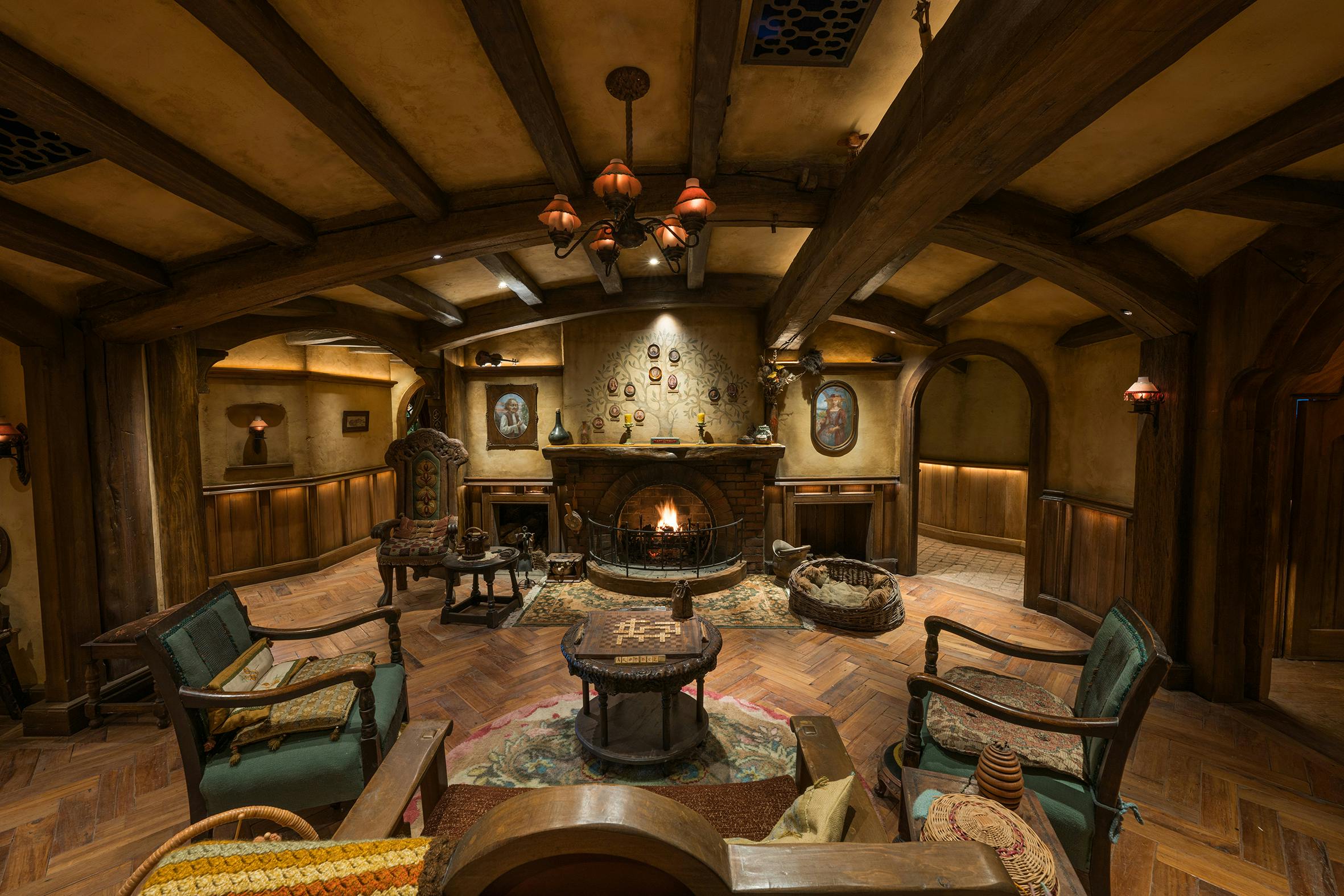 A cozy room with rustic furniture, a lit fireplace, wooden beams, and warm lighting, evoking a Hobbit-like ambiance.