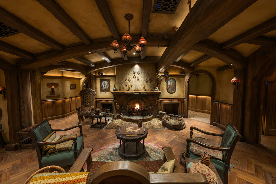A cozy room with a rustic design, featuring wooden beams, a fireplace, and comfortable chairs arranged around a central table.