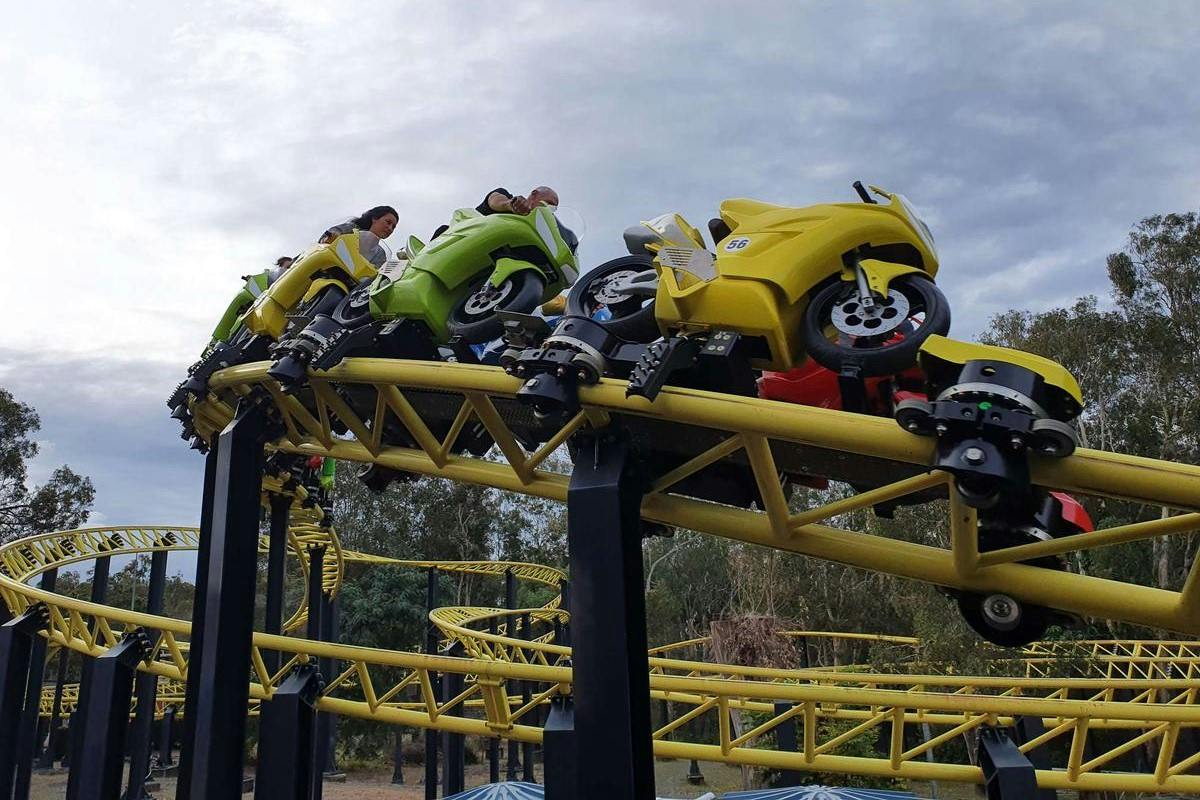A roller coaster featuring motorcycle-shaped cars on a yellow track, with a cloudy sky and trees in the background.