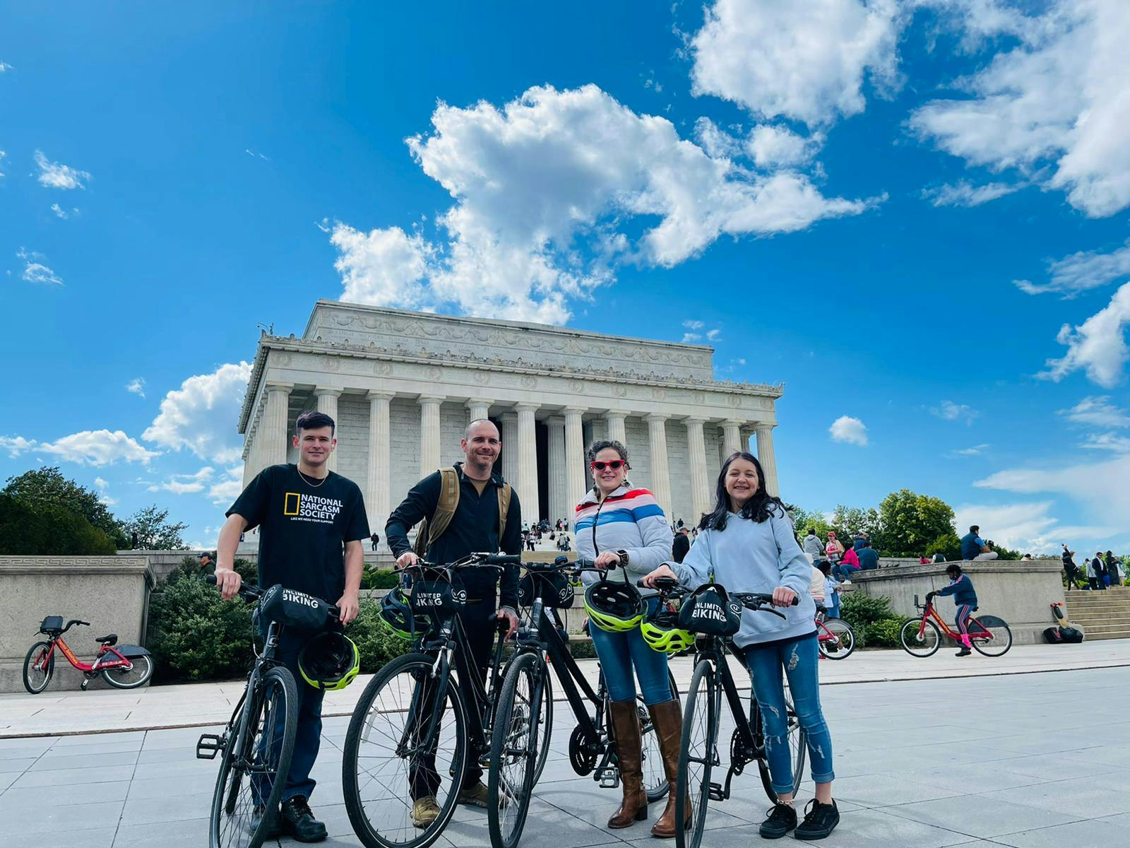 Quattro persone in bicicletta si trovano di fronte al Lincoln Memorial in una giornata di sole con un cielo azzurro e nuvole sparse.