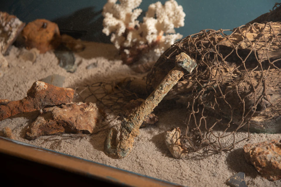 An underwater scene with a rusty anchor, fishing net, rocks, coral, and sand.