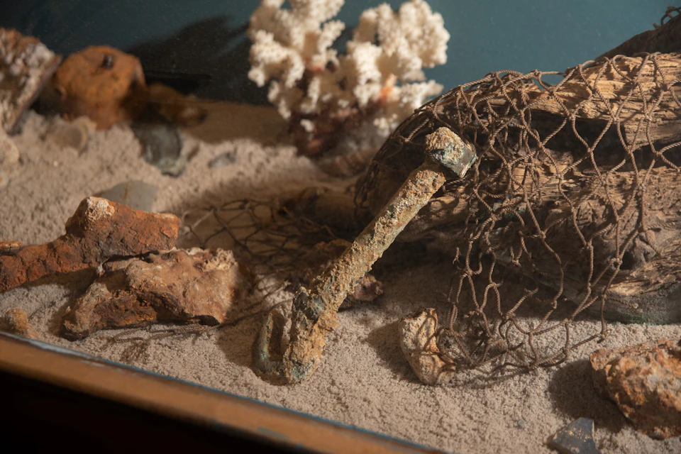 An underwater scene with a rusty anchor, fishing net, rocks, coral, and sand.