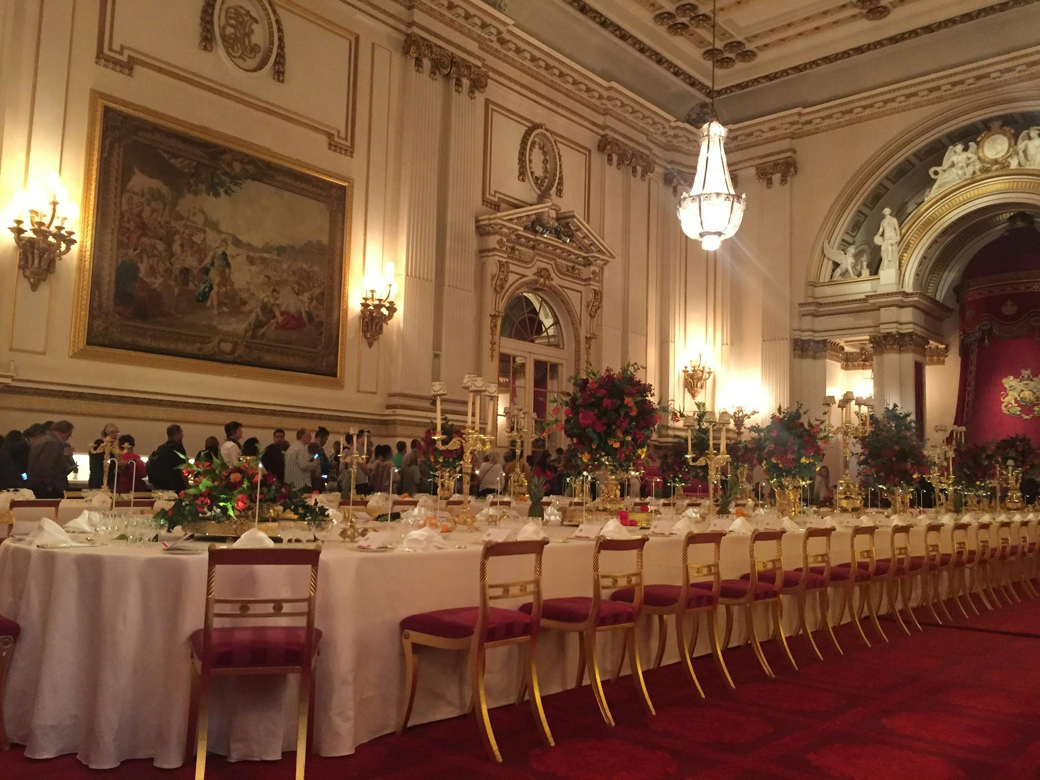 精心装饰的宴会厅，配有长餐桌、花卉中心摆件、红色椅子、吊灯和壁画。