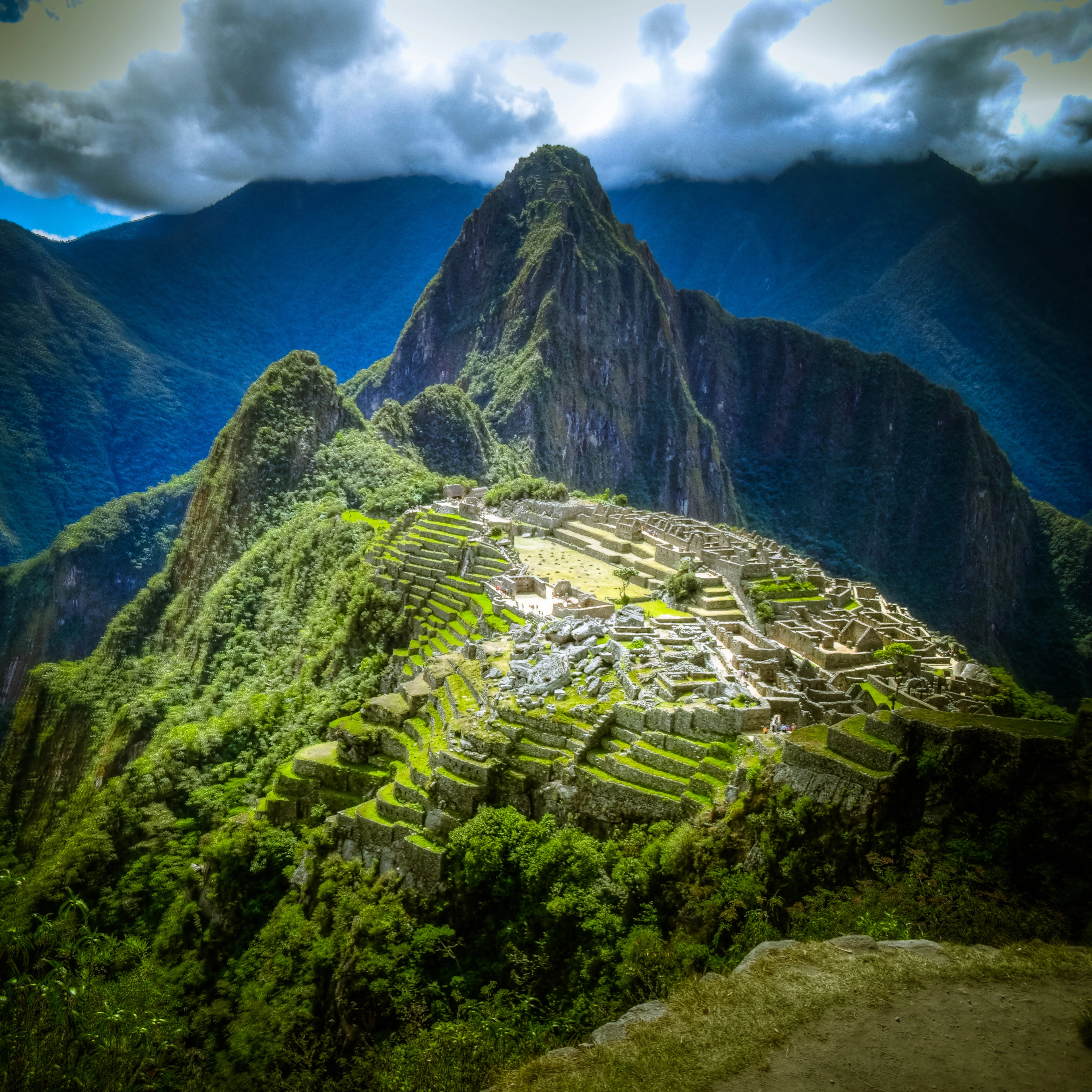 Ancient ruins of Machu Picchu nestled among lush, green mountains under a cloudy sky.