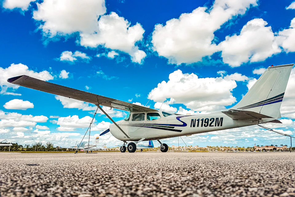 A small propeller plane with registration number N1192M is parked on a runway under a bright blue sky with scattered clouds.