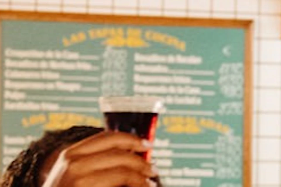 Three people raising glasses in a lively bar with hanging meats, bottles, and a menu on the wall.