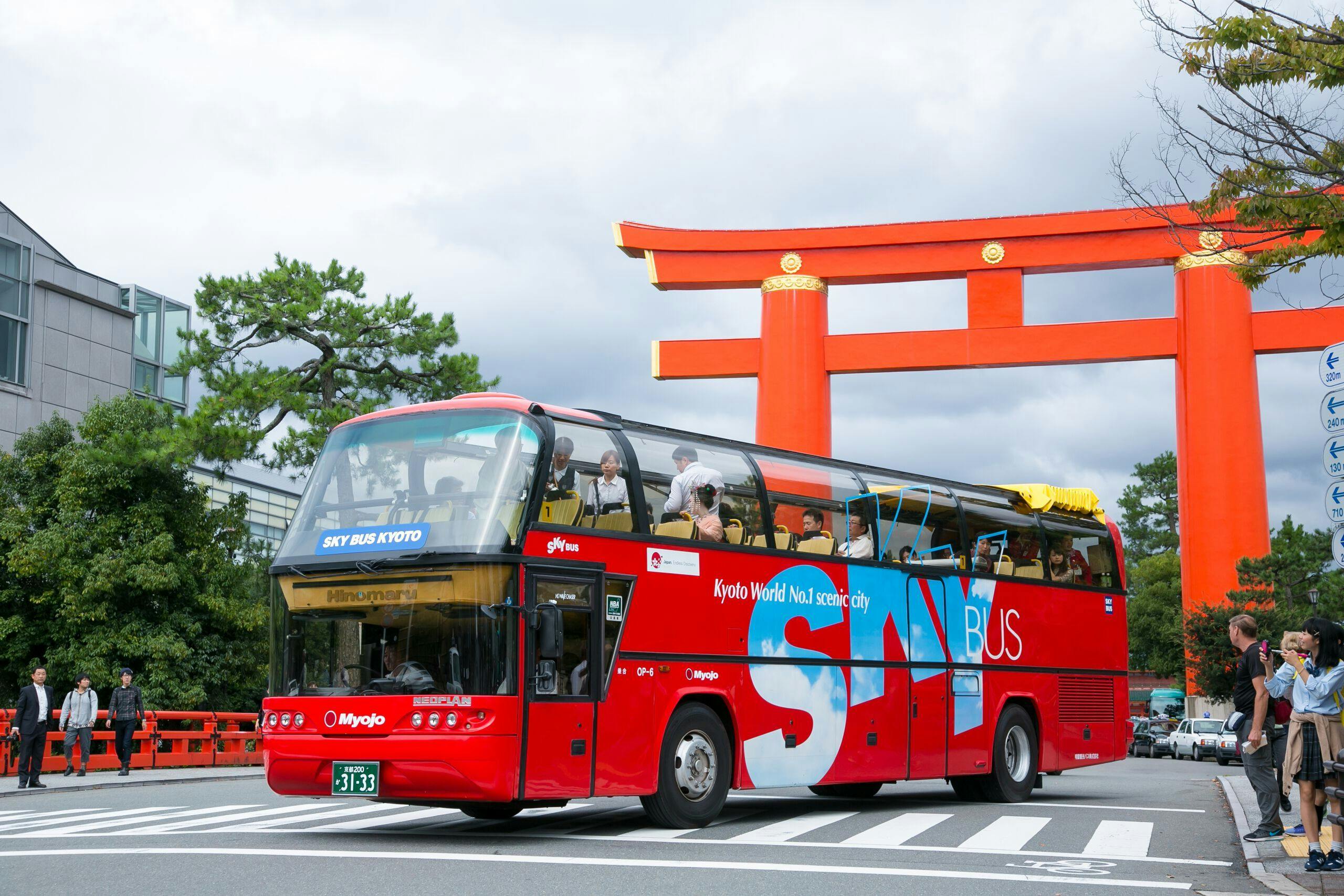 一辆标有「Sky Bus Kyoto」的红色双层巴士驶过大型橙色鸟居门。 巴士上可以看到游客。