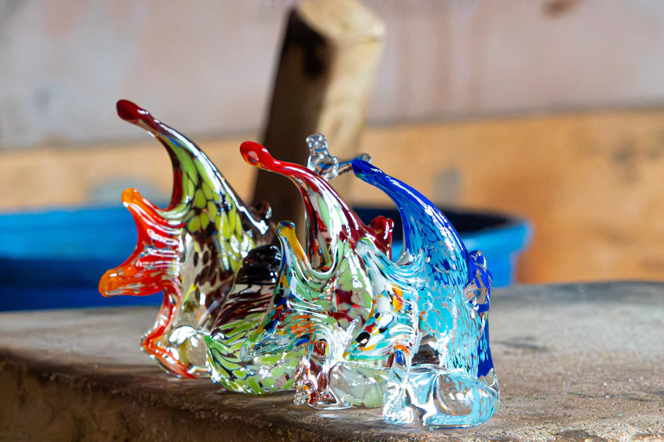 Colorful, intricately designed glass sculptures, resembling fish, displayed on a wooden surface. Blurred background.