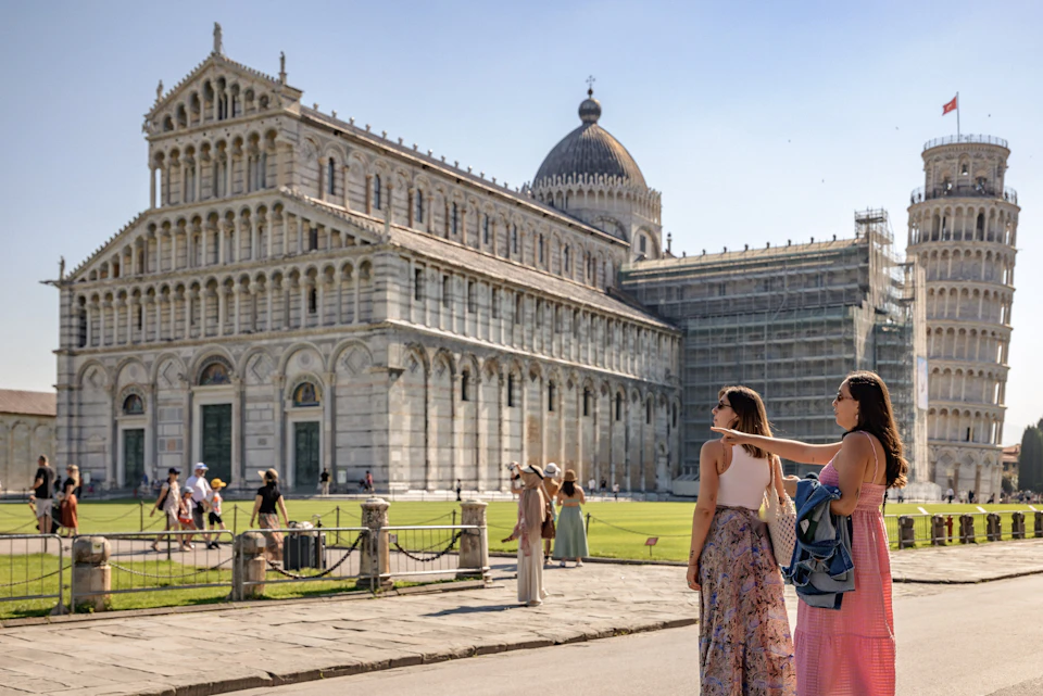 A historic cathedral with a dome stands in a sunny plaza as visitors walk and take photographs nearby.