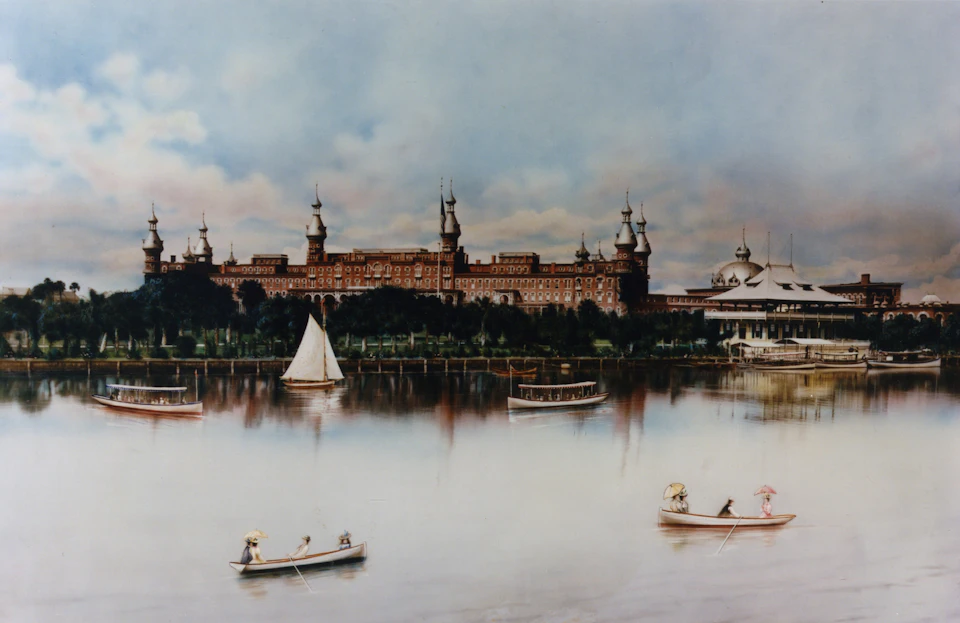 People in boats on a calm river with a large, ornate building and lush greenery in the background under a partly cloudy sky.