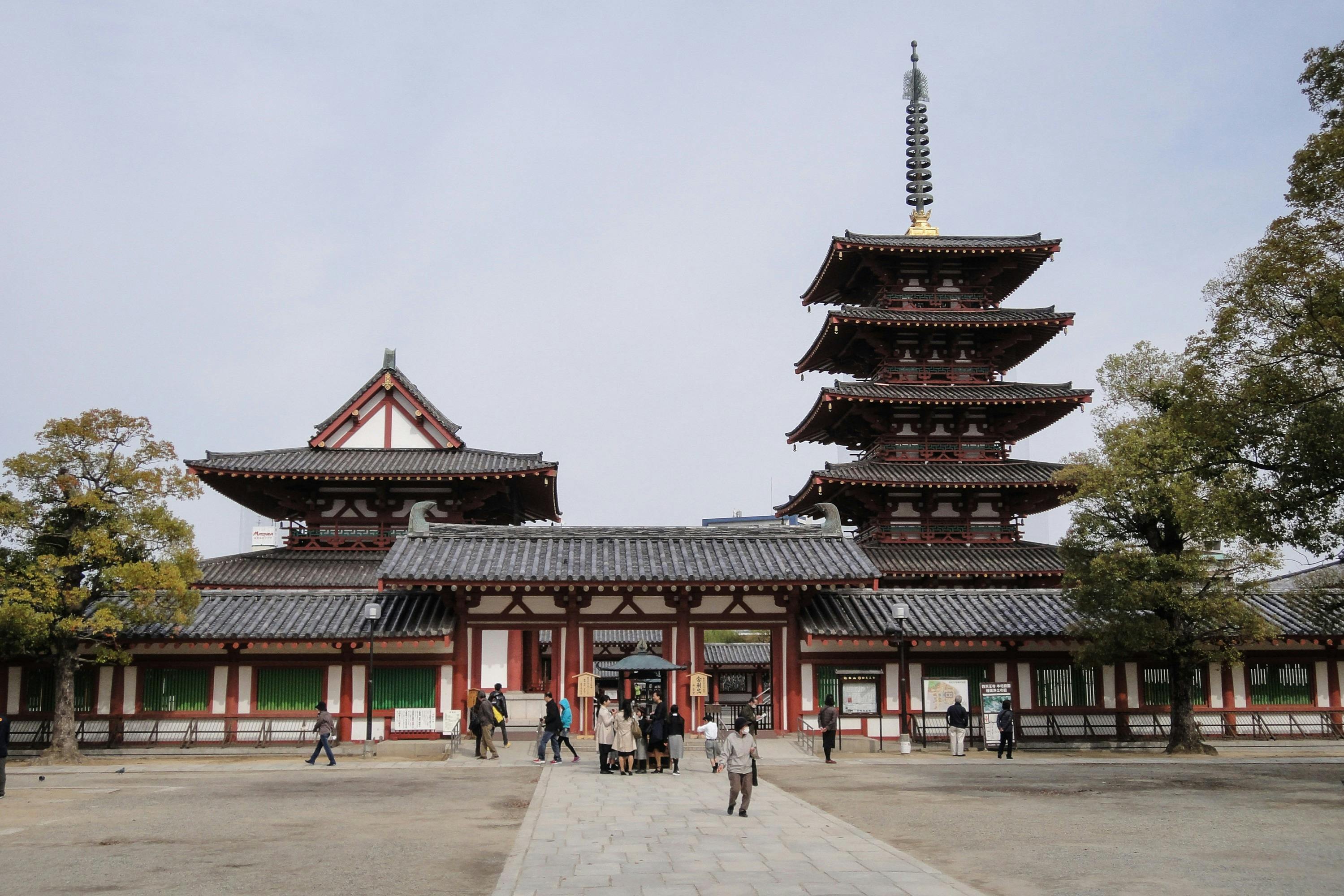 多層の塔と伝統的な建築物を持つ歴史的な日本の寺院の前を歩く人々。