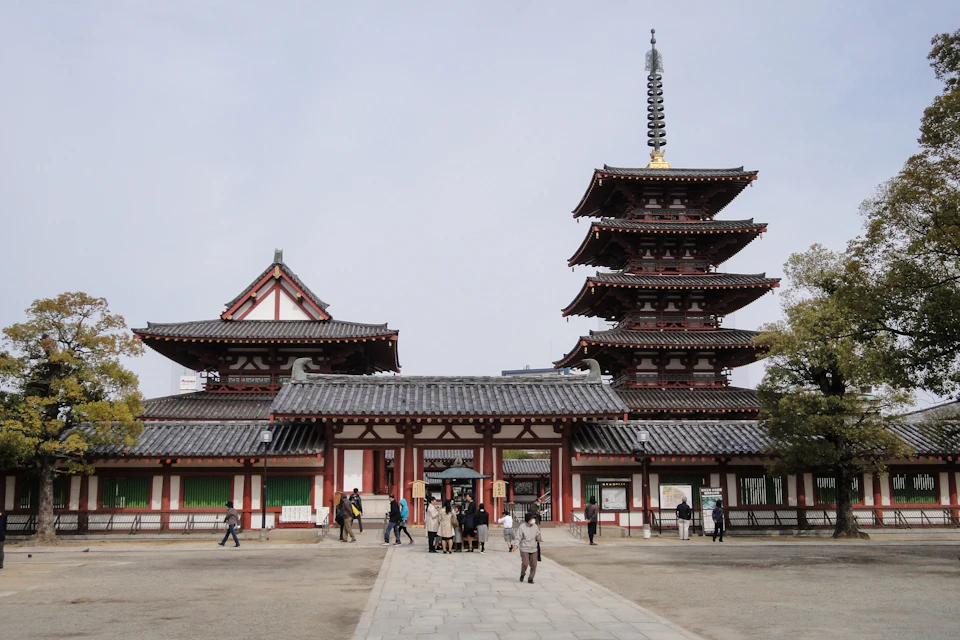 People walking in front of a historic Japanese temple with a multi-tiered pagoda and traditional architecture.