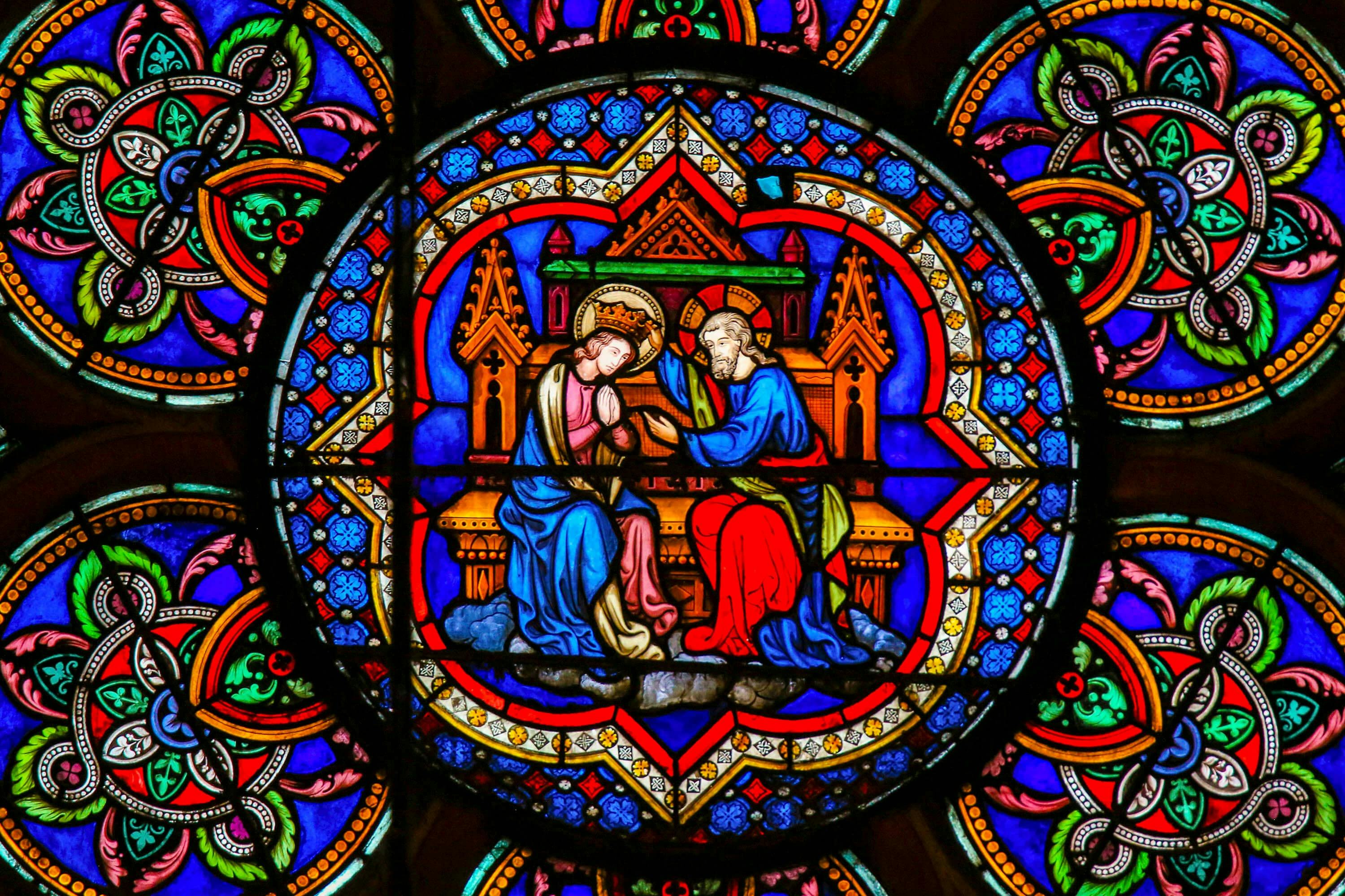 Ένα βιτρό παράθυρο που απεικονίζει δύο φωτοστέφανα με μπλε και κόκκινες ρόμπες, καθισμένα σε θρόνο με πολύχρωμο, περίτεχνο φόντο.