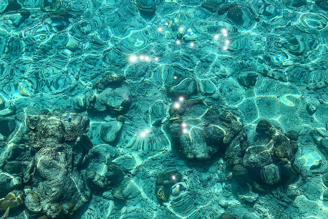 Κρυστάλλινα νερά με ηλιακό φως που δημιουργούν μια λαμπερή επίδραση στους υποβρύχιους βράχους.