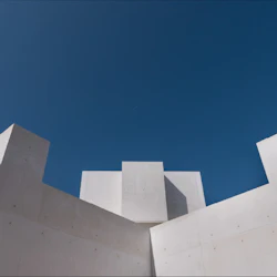 Vit geometrisk betongkonstruktion mot en klarblå himmel med moderna arkitektoniska linjer.