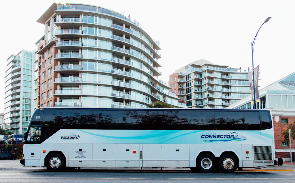 A coach bus labeled "BC Ferries Connector" is parked in front of modern high-rise buildings with curved facades.