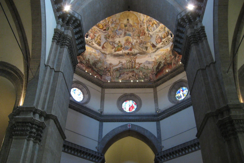 Interior of a cathedral dome with intricate frescoes and circular stained glass windows, viewed from below.