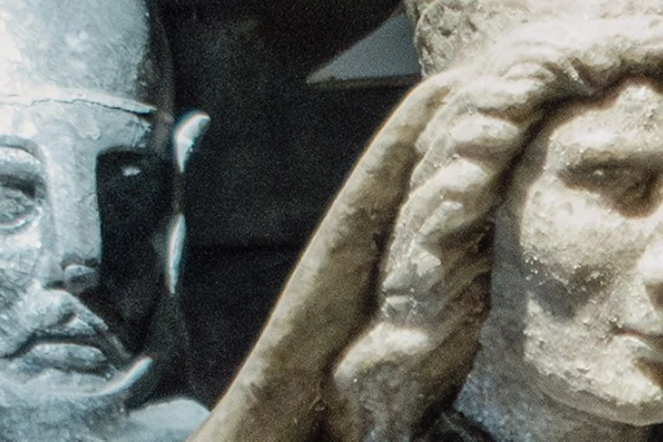 Stone statues of a medieval knight and a robed figure in a dimly lit setting, with a stone structure in the background.