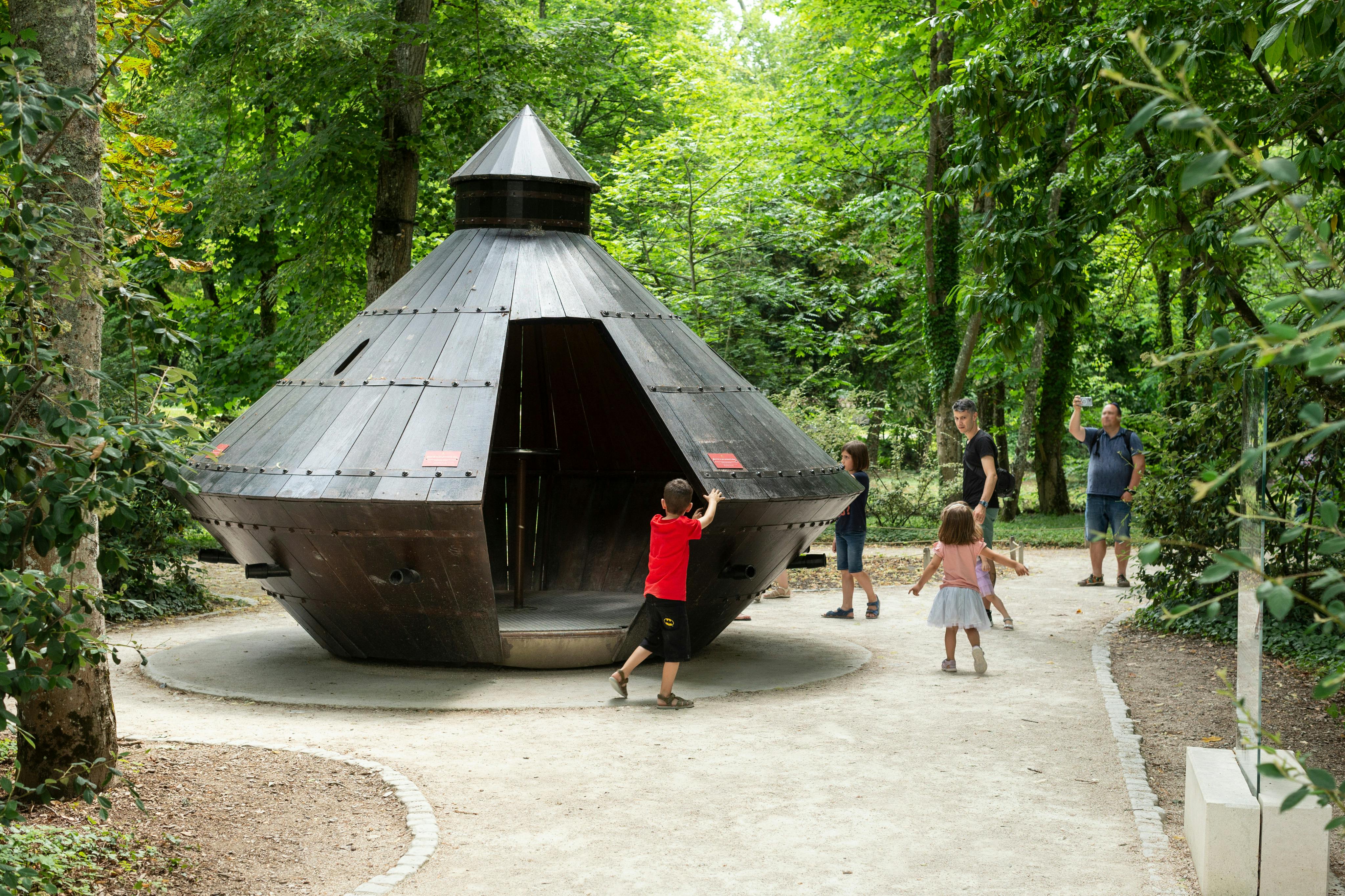 Niños y adultos se relacionan alrededor de una estructura de madera con forma de cúpula en un parque rodeado de árboles.