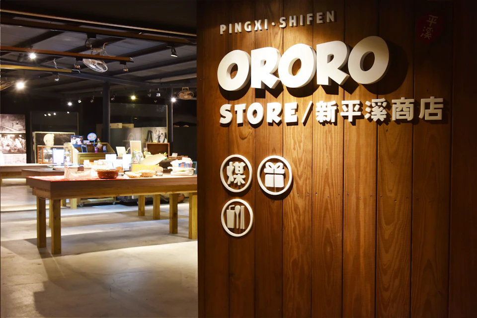 Interior of the ORORO store featuring a wooden wall with the store's illuminated name and a display of items on tables.