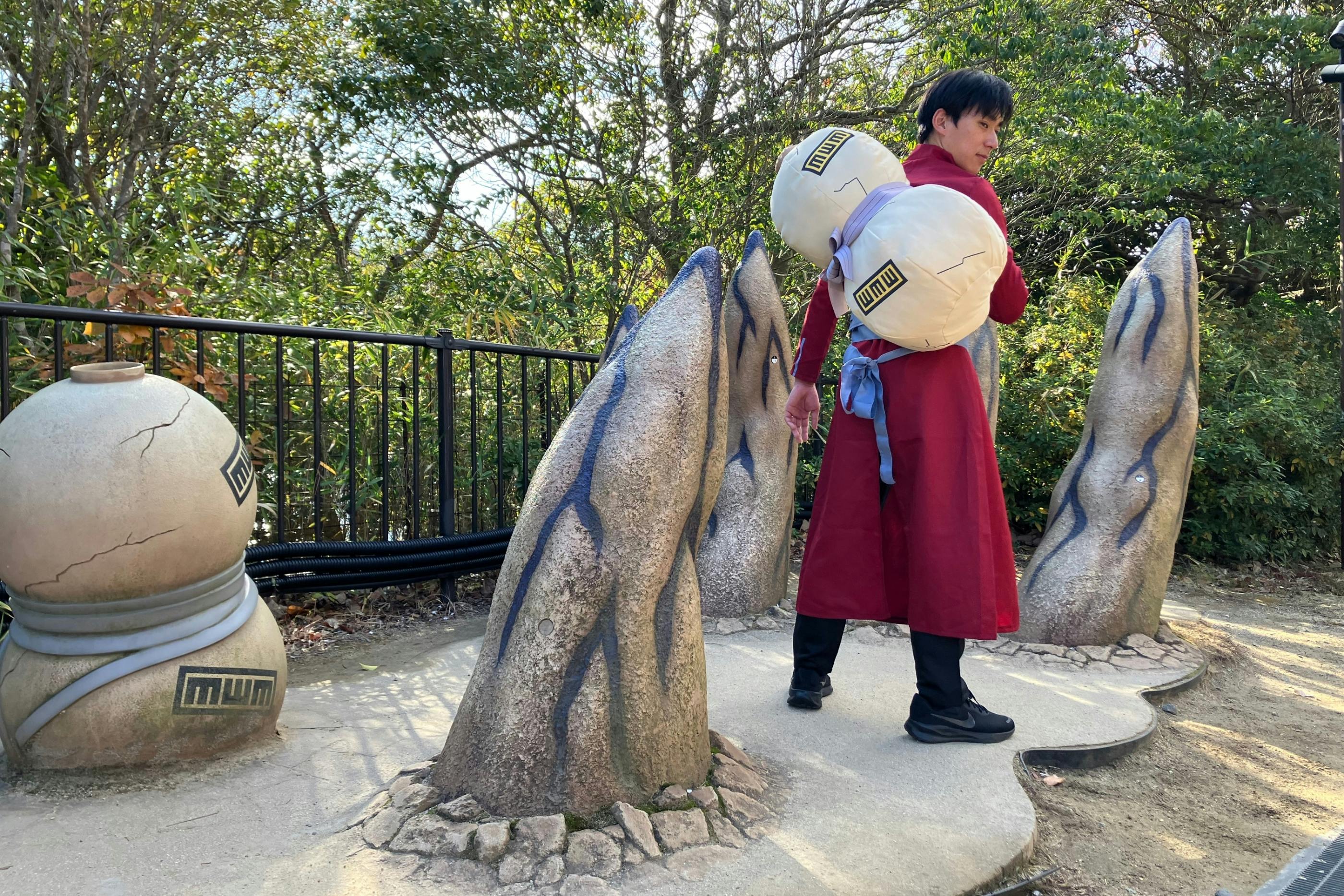 A person in a red outfit stands on a stone platform surrounded by pointed, rock-like structures in an outdoor setting.