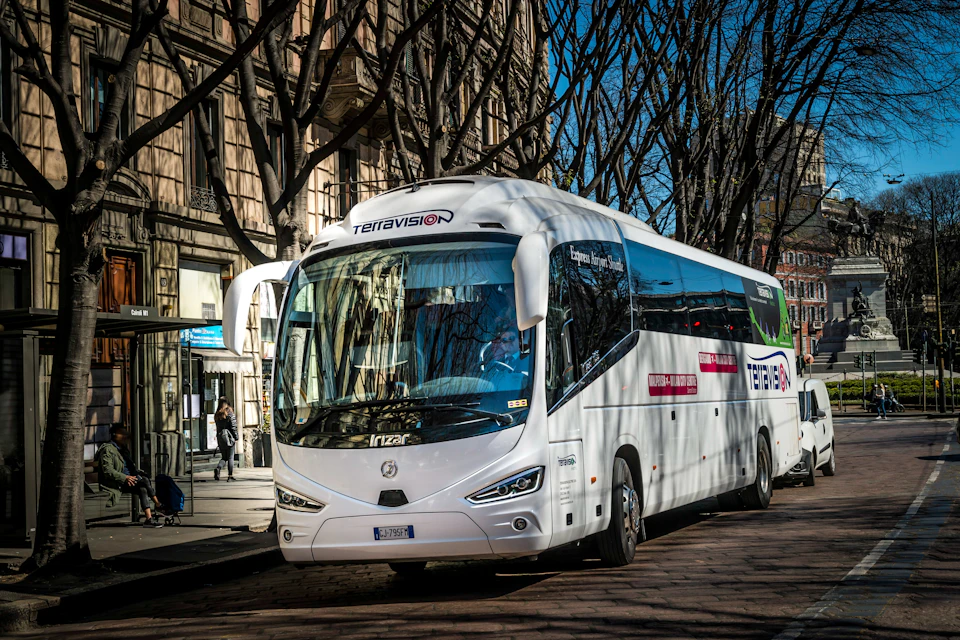 A white Terravision bus parked on a tree-lined street with buildings and a bus stop in the background.