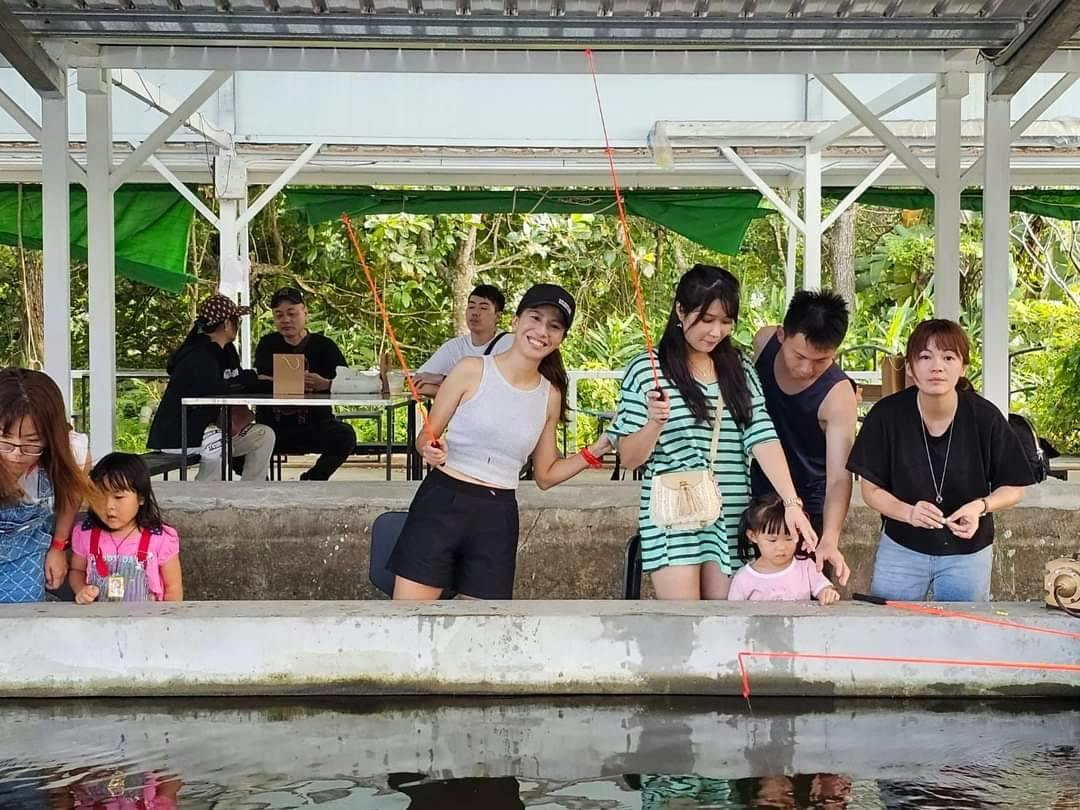 A group of people standing at a fishing pond under a shelter. Two are holding fishing rods, and a child is present.