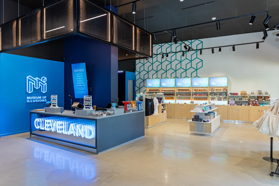 A modern retail store interior featuring a counter with illuminated signage, display shelves, and merchandise under bright lighting.