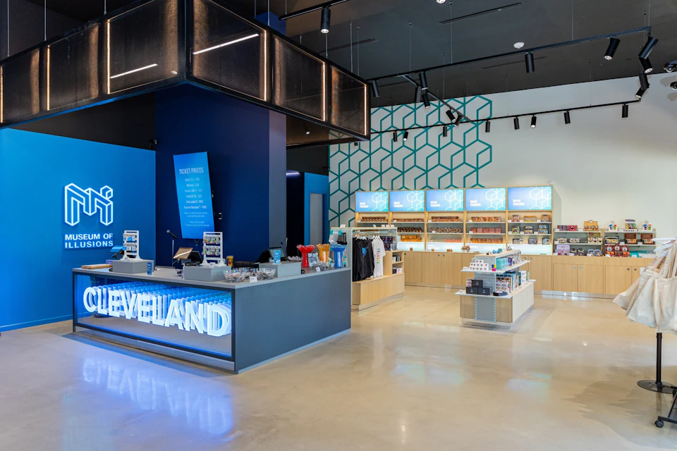 A modern retail store interior featuring a counter with illuminated signage, display shelves, and merchandise under bright lighting.