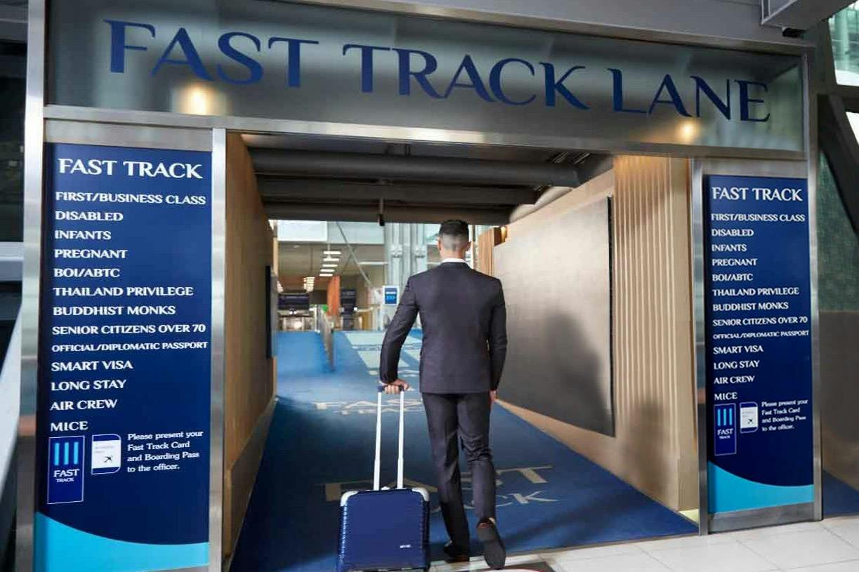 A person in formal attire pulling luggage enters an airport's Fast Track lane, with blue signage and carpeting visible.