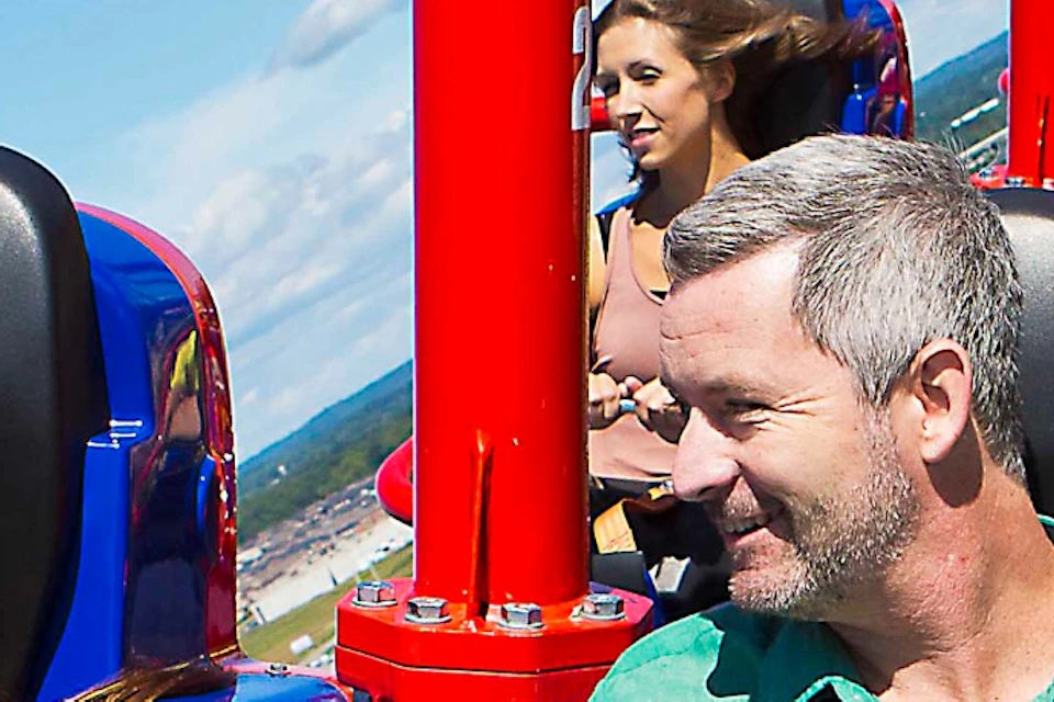 People enjoying a seated amusement park ride high above the ground, with landscapes visible in the background.