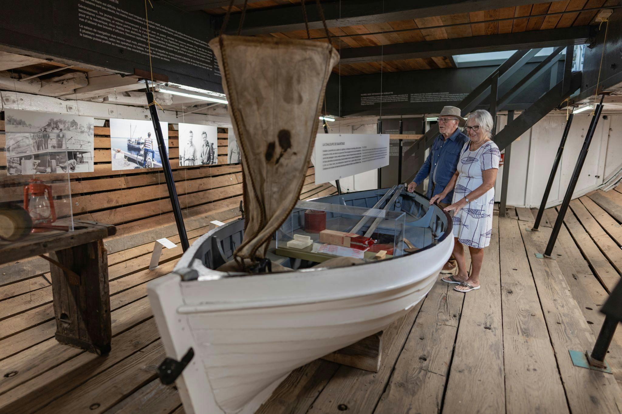 En ældre mand og kvinde undersøger en lille bådudstilling inde i et museum med trægulv og informationsskærme.