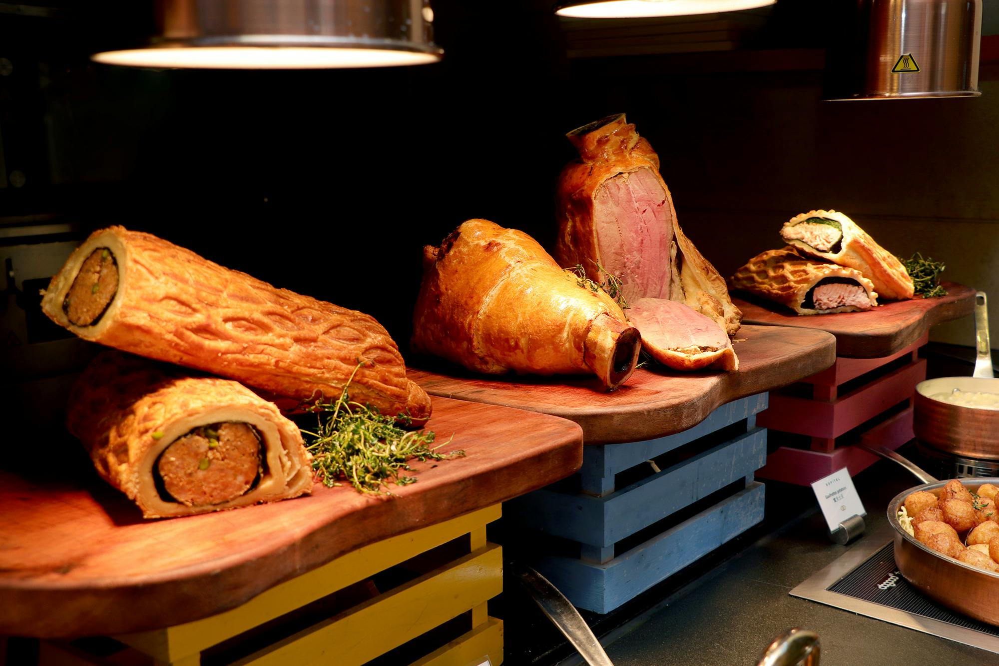 A variety of baked and roasted meats displayed on wooden boards, including a ham and pastry-wrapped items.