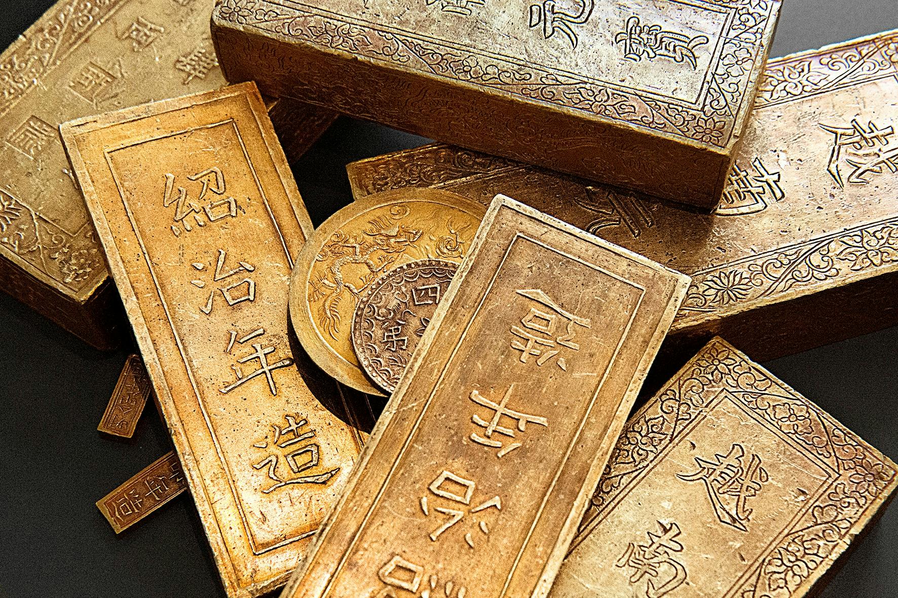 Χρυσές ράβδοι και νομίσματα με περίπλοκα χαρακτικά και κινεζικούς χαρακτήρες.