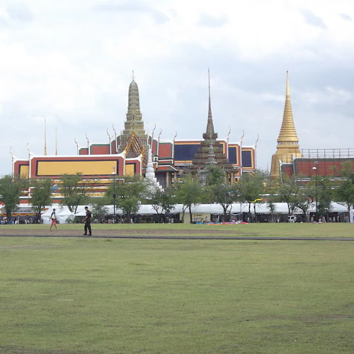 Verschnörkelte Tempelanlage mit roten und goldenen Dächern hinter einer grünen Wiese, mit zwei Personen im Vordergrund.