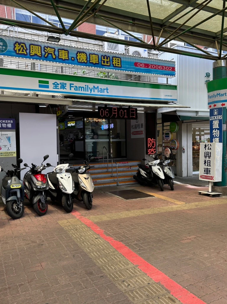 A FamilyMart convenience store entrance with a row of parked scooters in front, located on a tiled sidewalk.