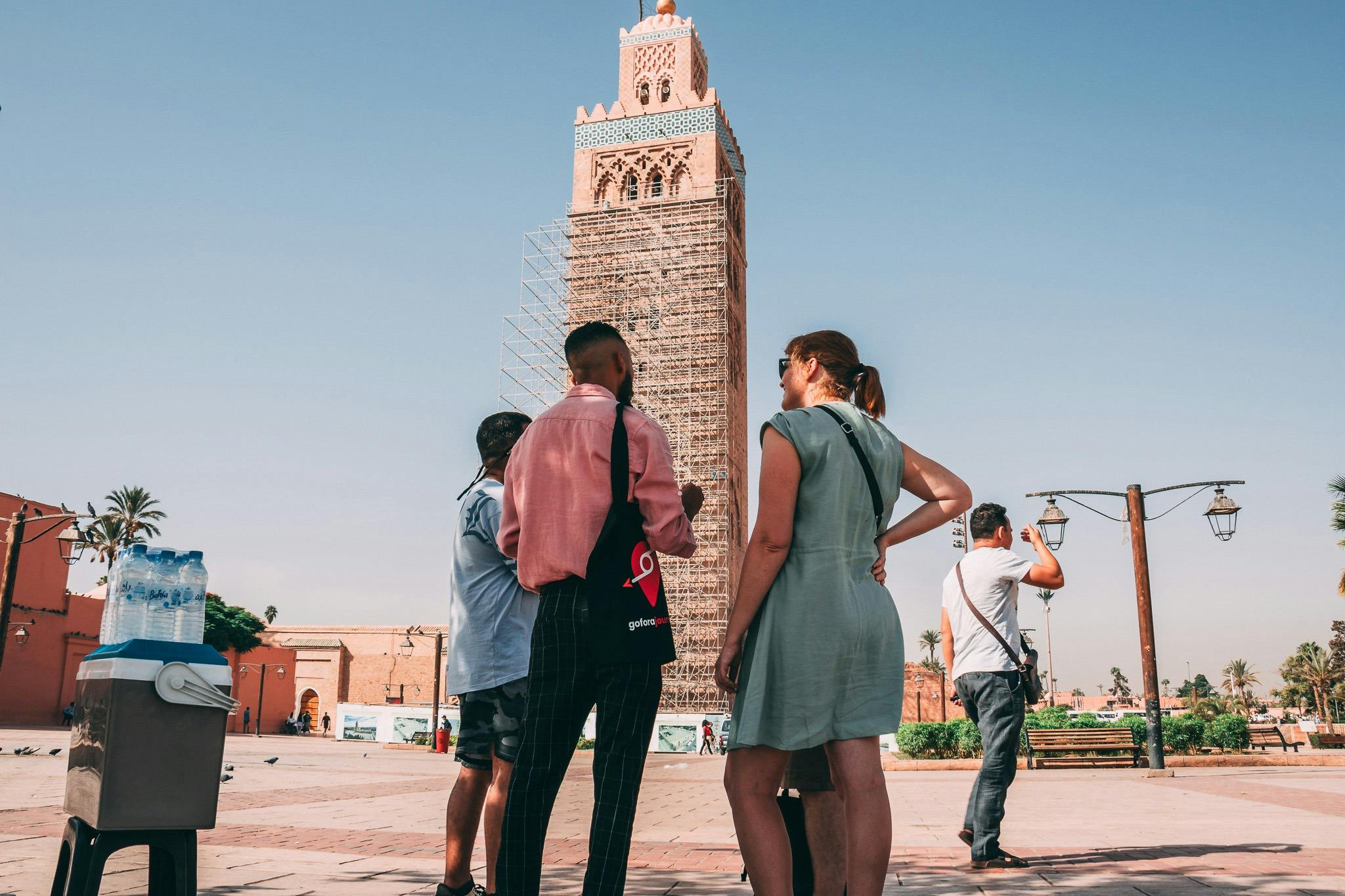 Οι άνθρωποι στέκονται και συνομιλούν μπροστά από έναν ψηλό, καλυμμένο με σκαλωσιές πύργο σε μια καθαρή μέρα.