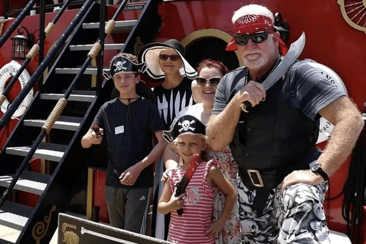 A group of people dressed in pirate-themed costumes posing together in front of a red ship.