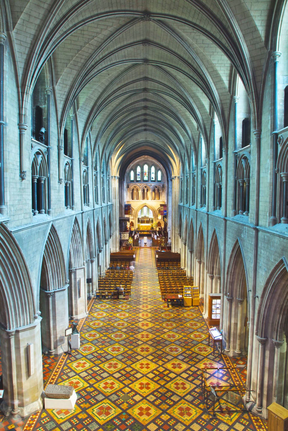 Interior of a large, ornate cathedral with high vaulted ceilings, arched columns, patterned floor, and wooden pews leading to the altar.