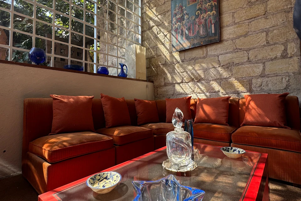 A cozy living room with a red sofa, glass-topped coffee table featuring decorative glassware, and a painting on a stone wall.