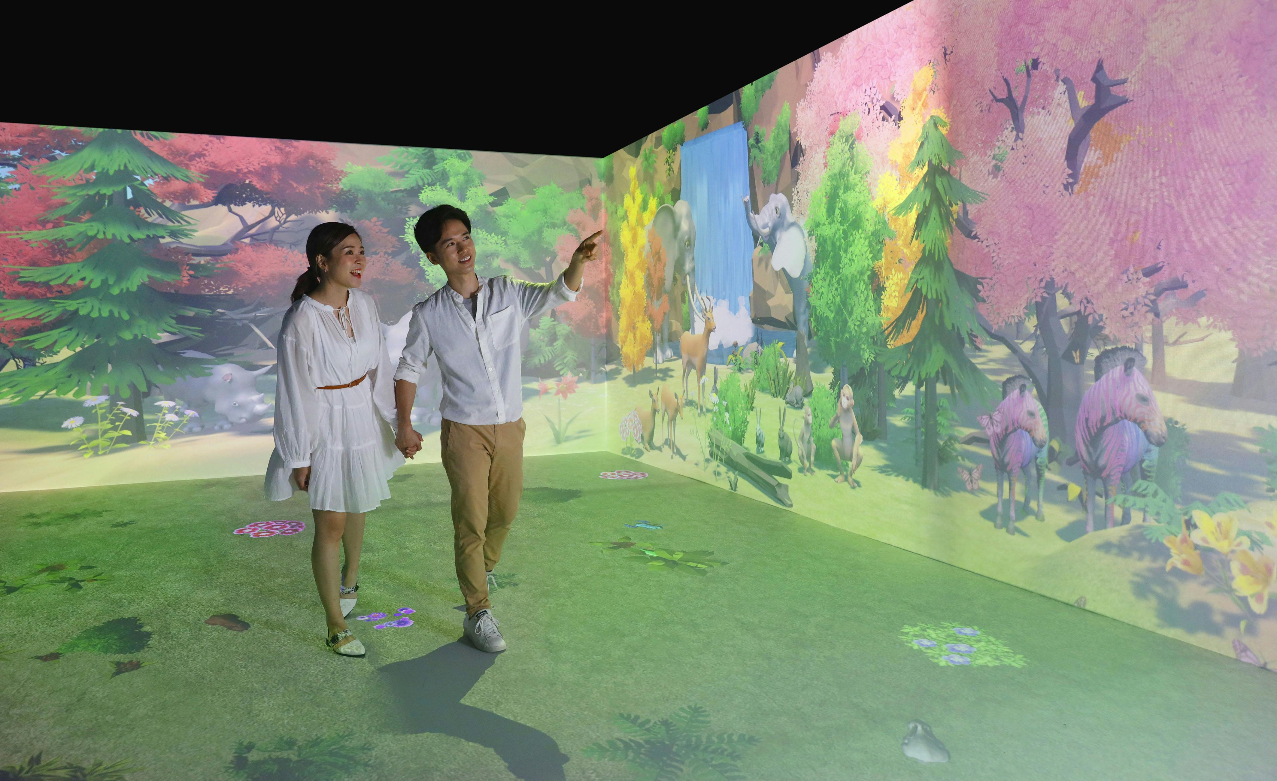 Пара держится за руки и улыбается, прогуливаясь по комнате с захватывающими цифровыми проекциями на природу.