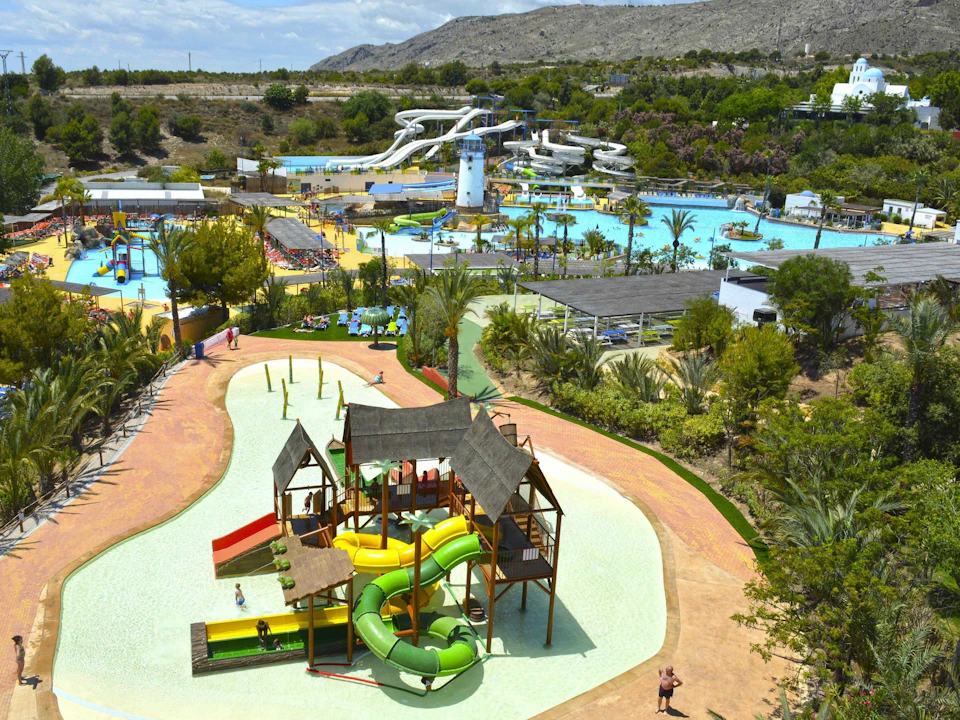 A water park with multiple water slides, pools, and play structures surrounded by greenery and mountains in the background.