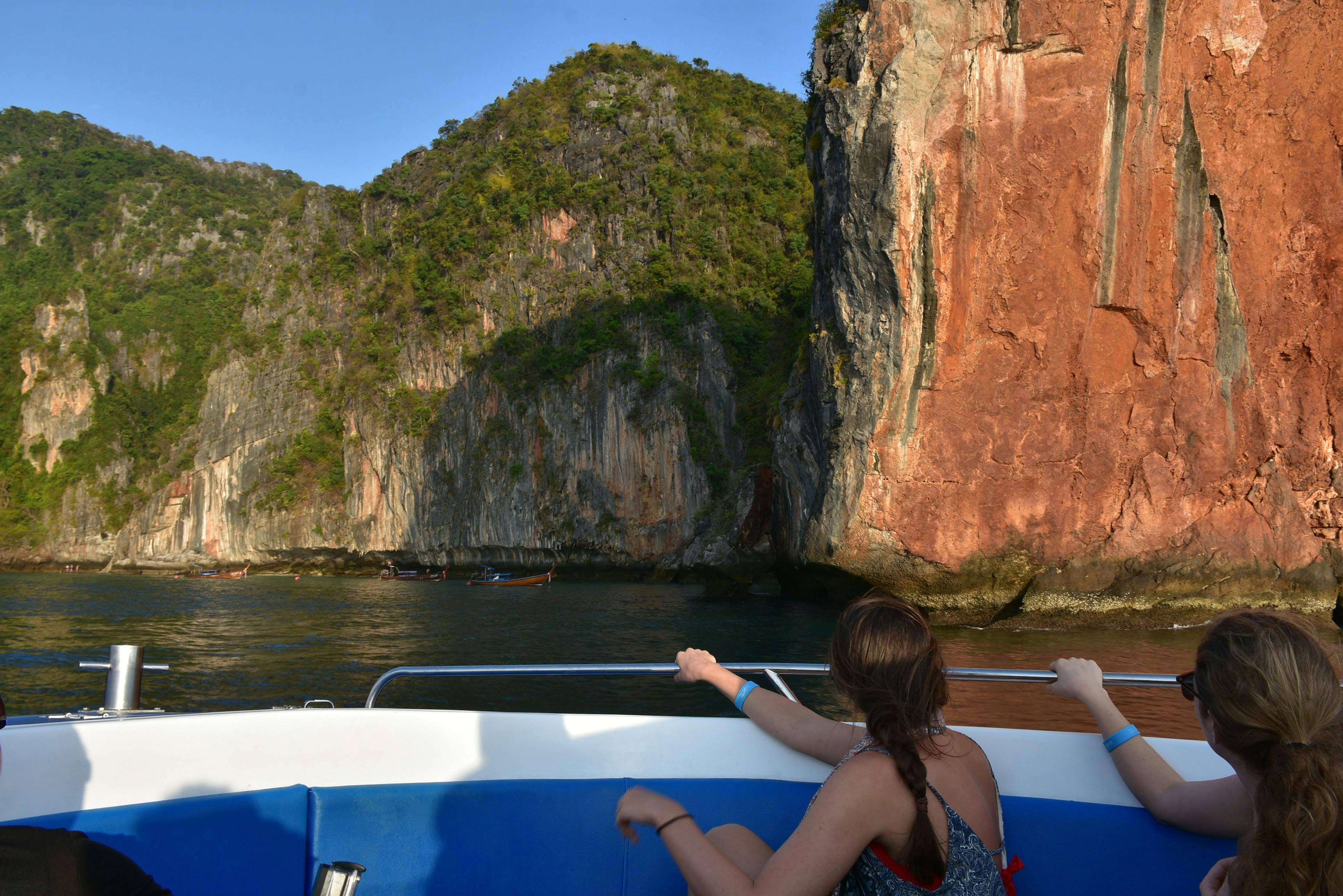 Ένα άτομο σε μια βάρκα κοιτάζει βραχώδεις βράχους και πράσινο κάτω από έναν καθαρό ουρανό.