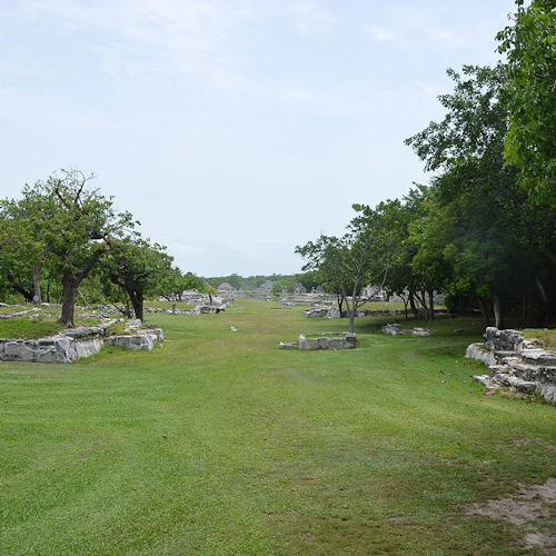 Alte Steinruinen, umgeben von Bäumen und Wiesen unter einem bewölkten Himmel.