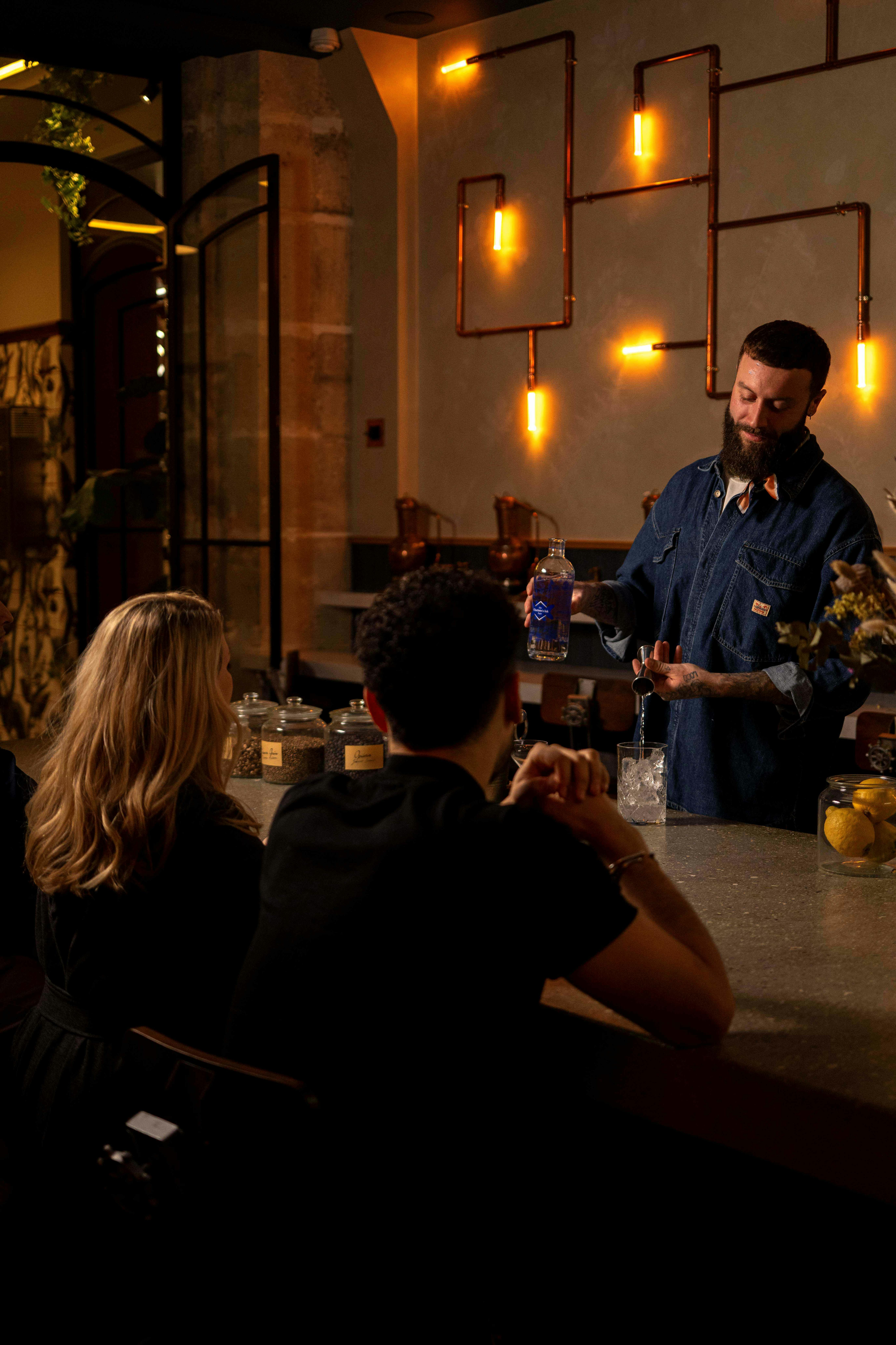 カウンターでドリンクを注ぐバーテンダー。暖かく明るいモダンなバーにお客様が座っています。