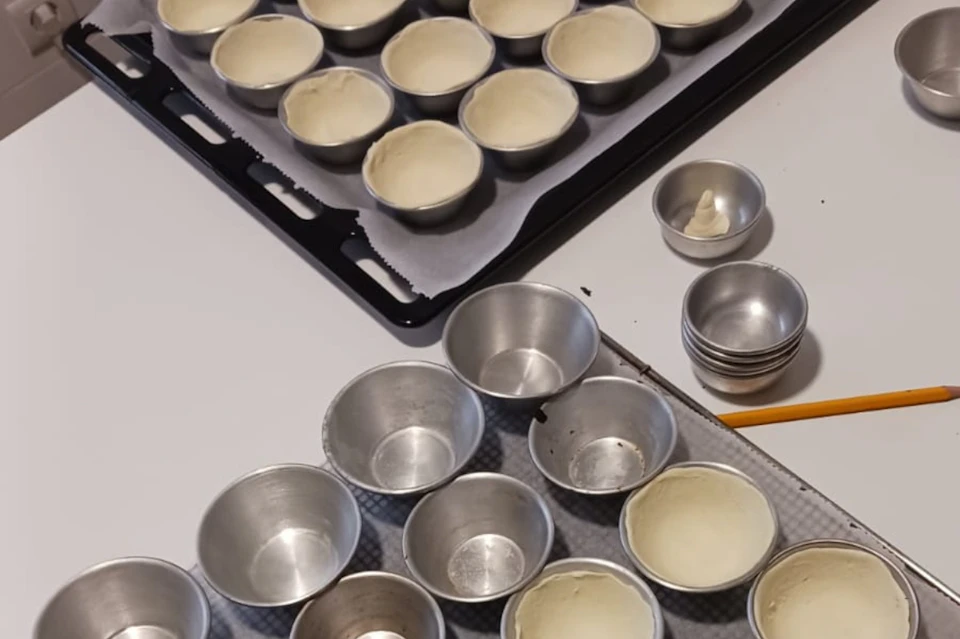 Metal baking molds are filled with dough, placed on a baking tray lined with parchment paper. Unused molds are nearby.