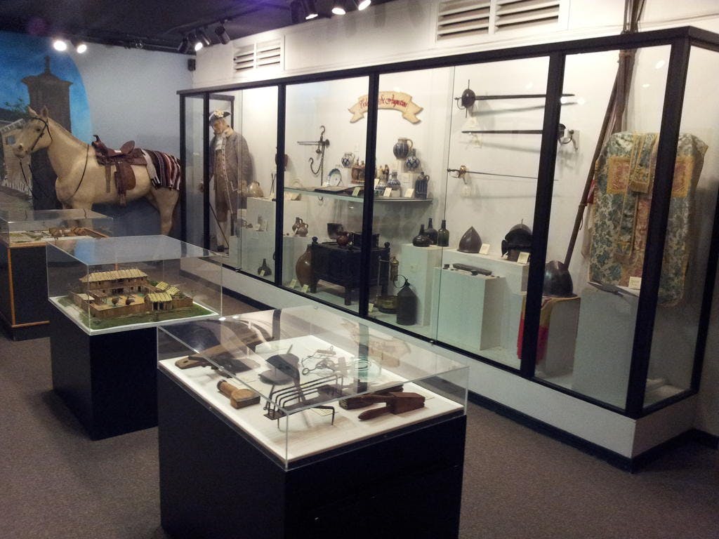 무기, 갑옷, 모형 등 역사적 유물이 전시된 박물관 전시관에는 말 마네킹과 마침표 의상을 입은 마네킹이 전시되어 있습니다.