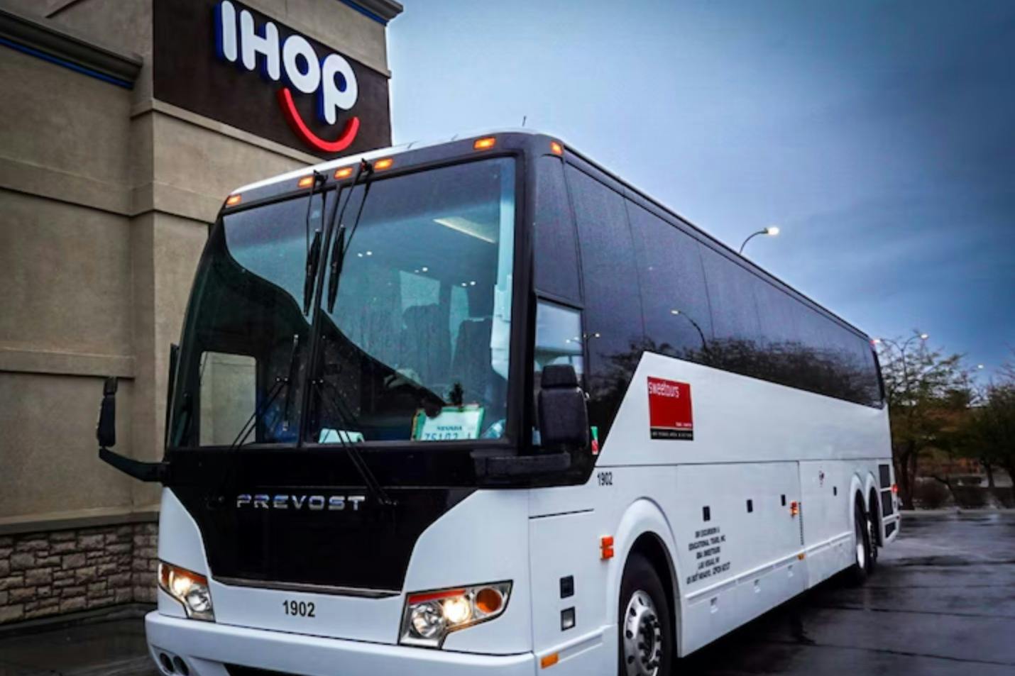 A white coach bus parked near an IHOP restaurant under a cloudy sky.